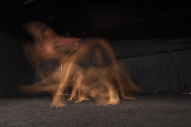 Eine etwas unscharfe Gruppe von Menschen auf einer Bühne mit schwarzem Hintergrund und einer Lampe oben drauf.