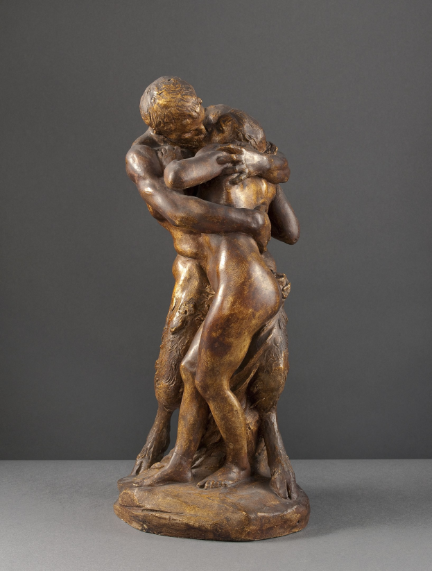 Bronzestatuette namens 'Der Kuss' von Jean-Baptiste-Camille Corot, die einen Mann in einem weißen Hemd und blauen Jeans zeigt, der eine Frau in einem orangefarbenen Kleid umarmt, mit detaillierten, lebensechten Details und einem warmen goldenen Ton gegen einen grauen Hintergrund.