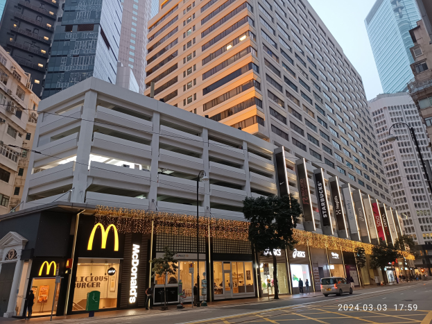 McDonald's-Restaurant auf einer belebten Stadtstraße mit hohen Gebäuden, Fahrzeugen, Fußgängern, Bäumen und einem klaren Himmel.
