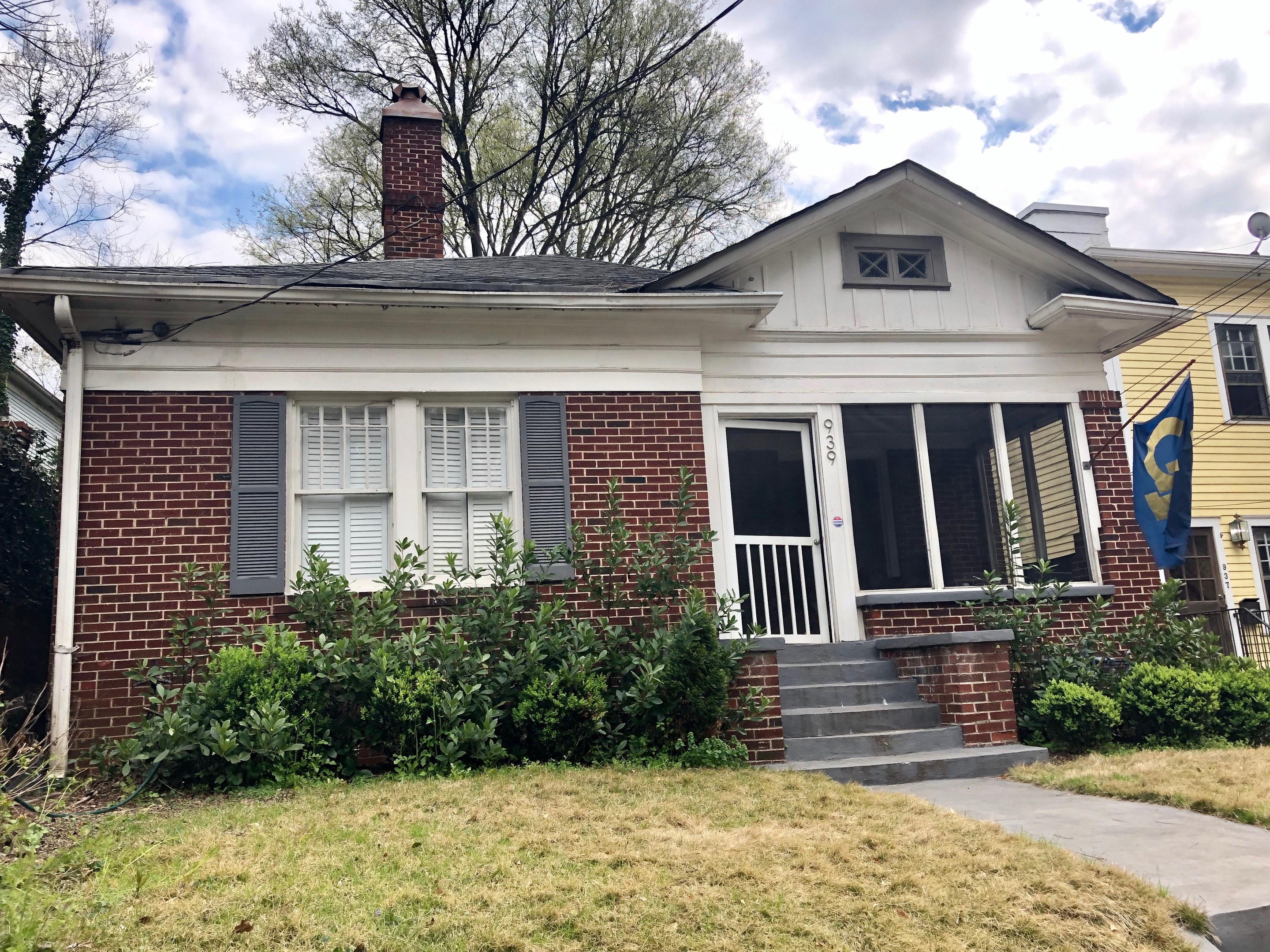 Backsteinhaus mit weißen Fensterläden und einer Flagge, umgeben von Pflanzen, Gras, einem Pfad, Bäumen, Drähten und einem bewölkten Himmel, gelegen an 030 E Main St, Nashville, TN 37211, verfügbar zur Miete mit der Listungs-ID 29058910.