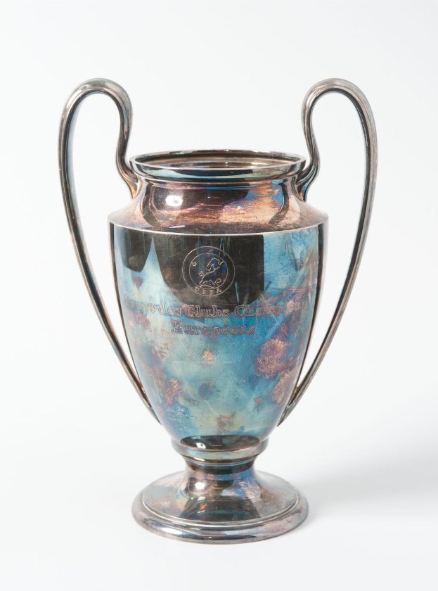 UEFA Champions League-Trophäe, ein stählerner Pokal mit zwei Griffen, blau und silbern in der Farbe, mit der Inschrift "UEFA Champions League" vor einem weißen Hintergrund.