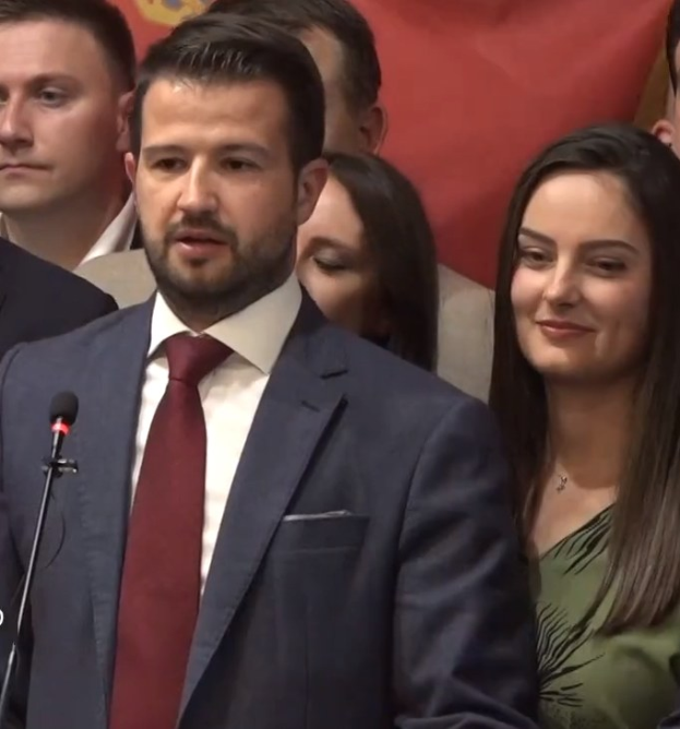 Ein Mann im Anzug spricht an einem Rednerpult mit einem Mikrofon zu einer Menge hinter einem Banner, wahrscheinlich über ein Regierungsverbot der Social-Media-Nutzung.