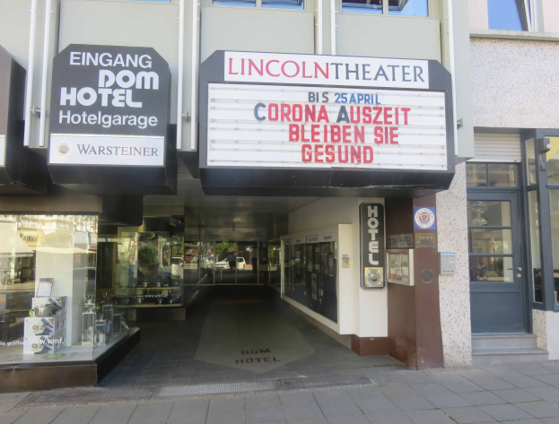 Außenansicht des Lincoln Theaters in Berlin, Deutschland, mit Glasfenstern und -türen, einem Schild und einer belebten Stadtkulisse im Inneren.
