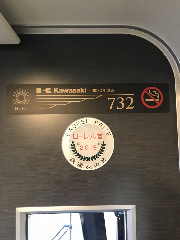 Eine Wand mit einem Schild, auf dem "Kawasaki 732" steht und ein Glasfenster auf der rechten Seite.