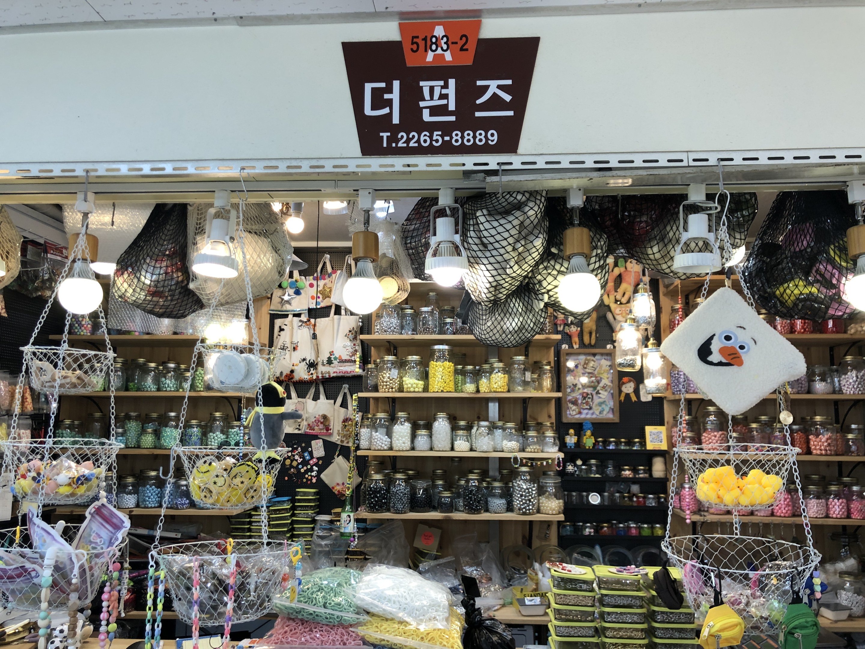 Ein unordentlicher Laden in Seoul mit verschiedenen Artikeln wie K%C3%B6rben, Lichtern, Flaschen und Spielzeugen auf Regalen, mit einer Tafel oben, die anzeigt, dass es ein Top-bewerteter koreanischer Shop ist.