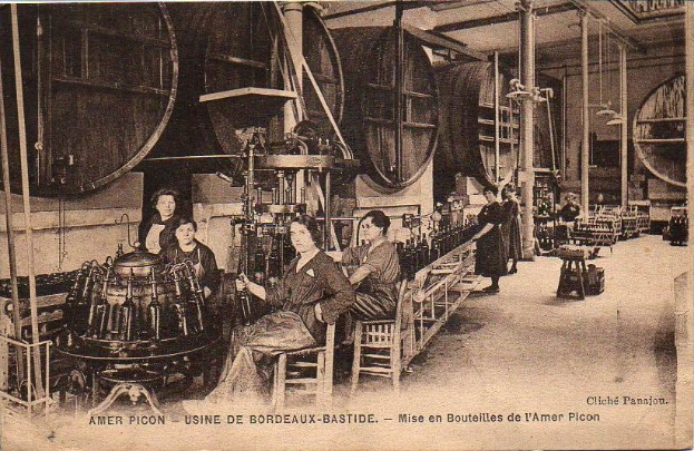 Ein Schwarz-Weiß-Foto von Frauen, die in einer Fabrik arbeiten, mit einigen sitzend und anderen stehend zwischen Maschinen, und Text unten, der 'Amer Picon - Use de Bordeaux-Bastide' liest.
