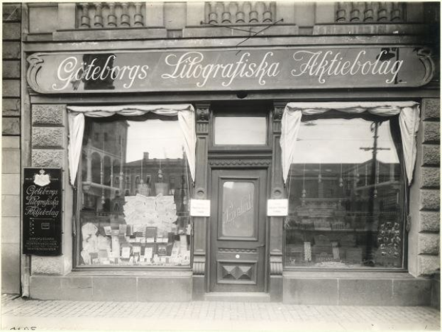 Schwarzes und weißes Foto einer Geschäftsfront mit einer Tür, Fenstern, Vorhängen und einem Schild mit der Aufschrift "Giteborgs Litografiska Aktiebolag" in Stockholm, Schweden.