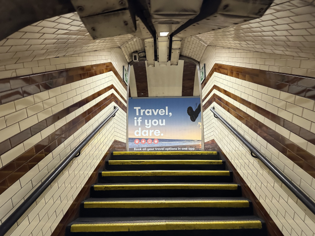 Eine Treppe in einer U-Bahn-Station mit Geländern auf beiden Seiten, die zu einem Schild führt, das "Reise, wenn du wagst" lautet.