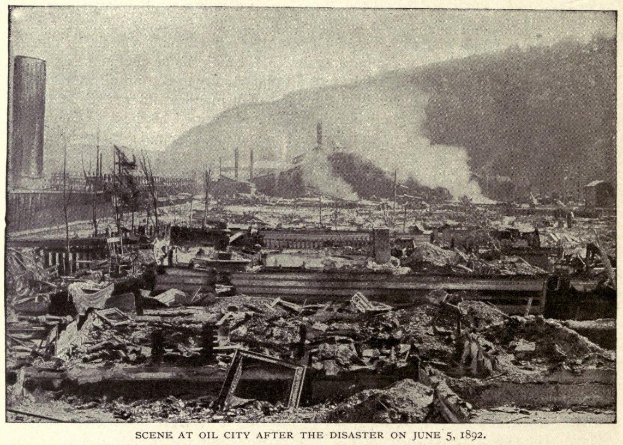 Schwarz-weiß-Foto einer Stadt nach einer Katastrophe am 5. Juni 1892, das beschädigte Gebäude, Strommasten, Rauch und einen Hügel im Hintergrund zeigt.