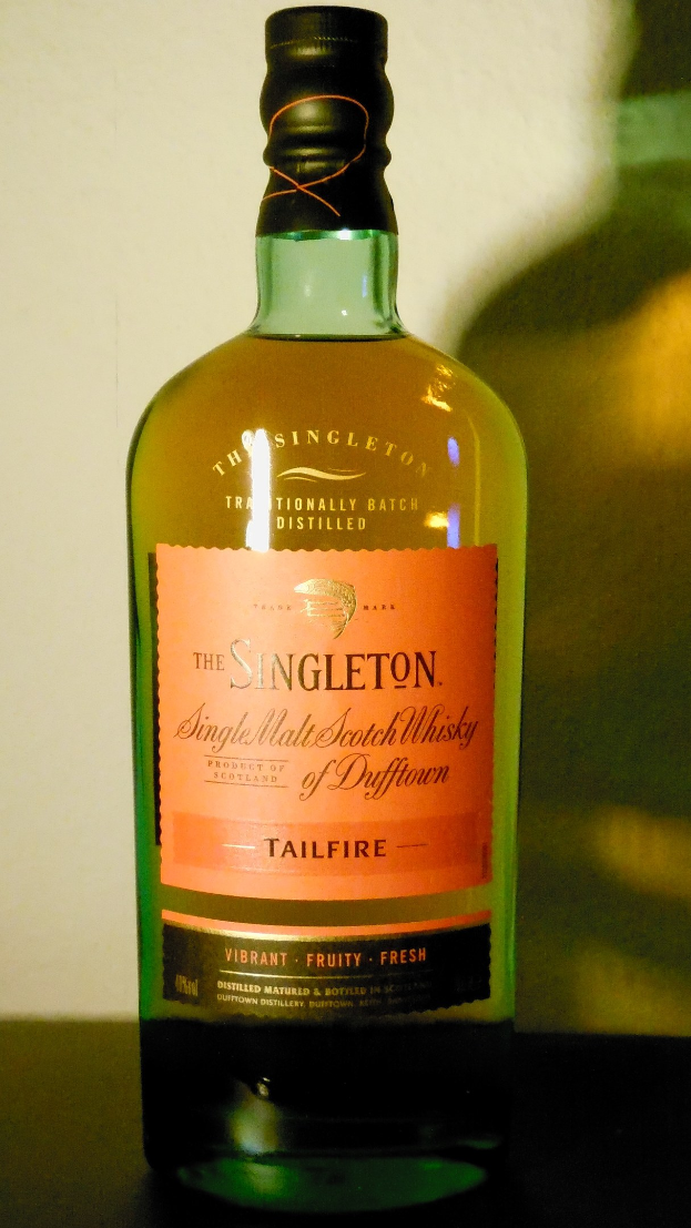 Eine tiefe bernsteinfarbene Flasche Singleton of Dufftown Tailfire Single Malt Scotch Whisky mit einem schwarzen Etikett, das ein Wappen mit einem Löwen und einem Schloss zeigt.