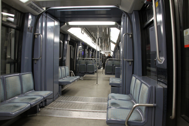 Innenraum eines U-Bahn-Zugs mit blauen Sitzen, Türen, Griffen, Stangen, Lampen und anderen Gegenständen, der ein paar Menschen in einer belebten Stadtlandschaft zeigt.