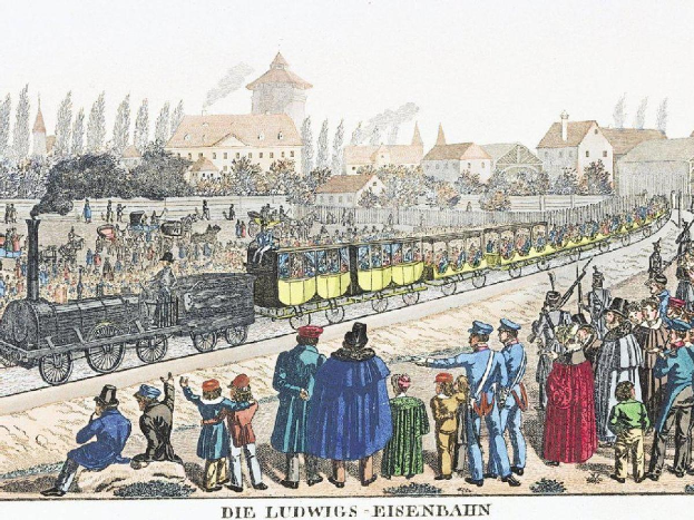 Gruppe von Menschen um einen Zug auf Schienen mit einigen Passagieren im Zug und anderen außerhalb, mit Gebäuden und Bäumen im Hintergrund und dem Text "Ludwigs-Eisenbahn, der erste Bahnhof in Deutschland" unten.