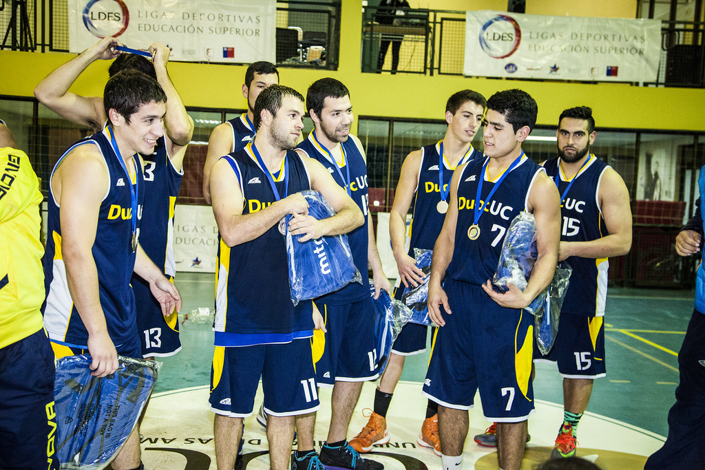 Eine Gruppe von Menschen, einige mit Medaillen und Gegenständen in den Händen, steht vor Bannern und Geländern.