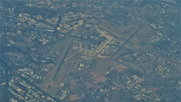 Luftaufnahme eines Flughafens umgeben von städtischer Infrastruktur, mit Text unten.