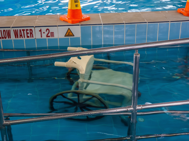 Schwimmbad mit einem Stuhl in der Mitte, umgeben von Sicherheitstonnen und einem Geländer und einem Schild an der Wand, das verfügbare Schwimmausrüstung anzeigt.