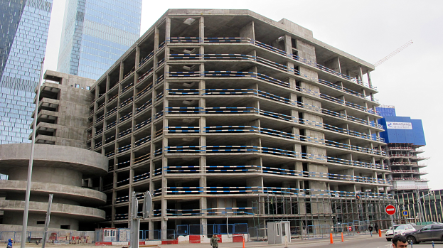 Großes Bauprojekt in einer von Wolkenkratzern umgebenen Stadt mit Fahrzeugen, Fußgängern, Verkehrsinfrastruktur und Kränen vor einem klaren Himmel.