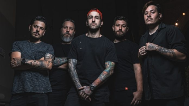 Eine Gruppe von Männern, die in einem dunklen Raum stehen, von rechts beleuchtet, während eines Interviews, das wahrscheinlich für Avenged Sevenfold stattfindet.