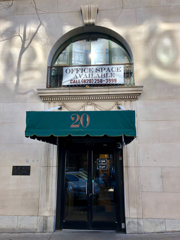 Gebäude mit einer Glastür, einer grünen Markise und einem Schild mit der Aufschrift "Büroräume zu vermieten" an der Vorderseite; enthält ein Geländer, einen Baum links und eine Tafel mit Text.