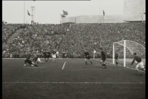 Ein Schwarz-Weiß-Foto eines Fußballspiels im Stadion, mit Spielern auf dem Feld und einem Torpfosten auf der rechten Seite, Zuschauern in den Rängen und Fahnen mit Stangen im Hintergrund, mit Text oben und unten '1958-1958 WM-Finale - Manchester United v Liverpool'.
