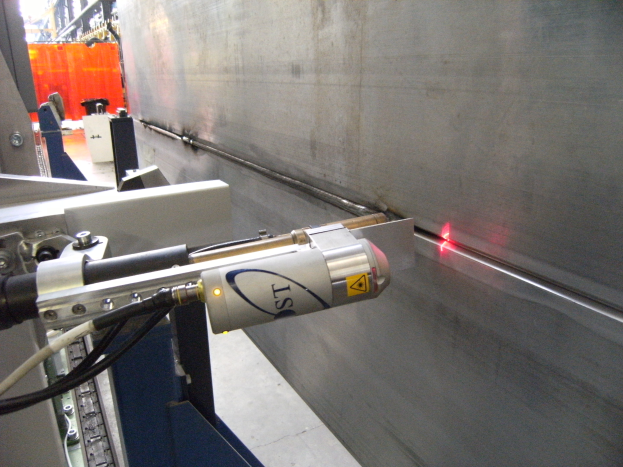 Heller Laserstrahl aus einer Schneidemaschine in einer Fabrik, der die Umgebung erhellt, mit einer Wand auf der rechten Seite und Hintergrundobjekten.