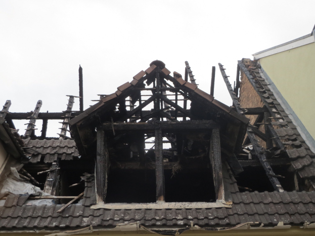Ein Gebäude mit einem durch Feuer beschädigten Dach wird abgerissen, Trümmer einschließlich Holzplanken sind über das Gelände verstreut.