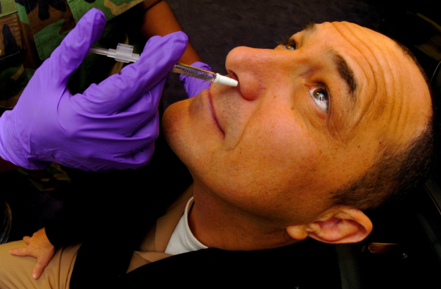 Ein Arzt in lila Handschuhen spritzt einem Mann ein Vakzin in den Mund mit einer Spritze.