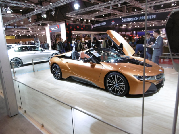Ein elegantes schwarzes BMW i8 Roadster mit Chromakzenten und einem modernen Innenraum, das auf der Internationalen Automobil-Ausstellung in Frankfurt präsentiert wird und von formell gekleideten Besuchern umgeben ist.