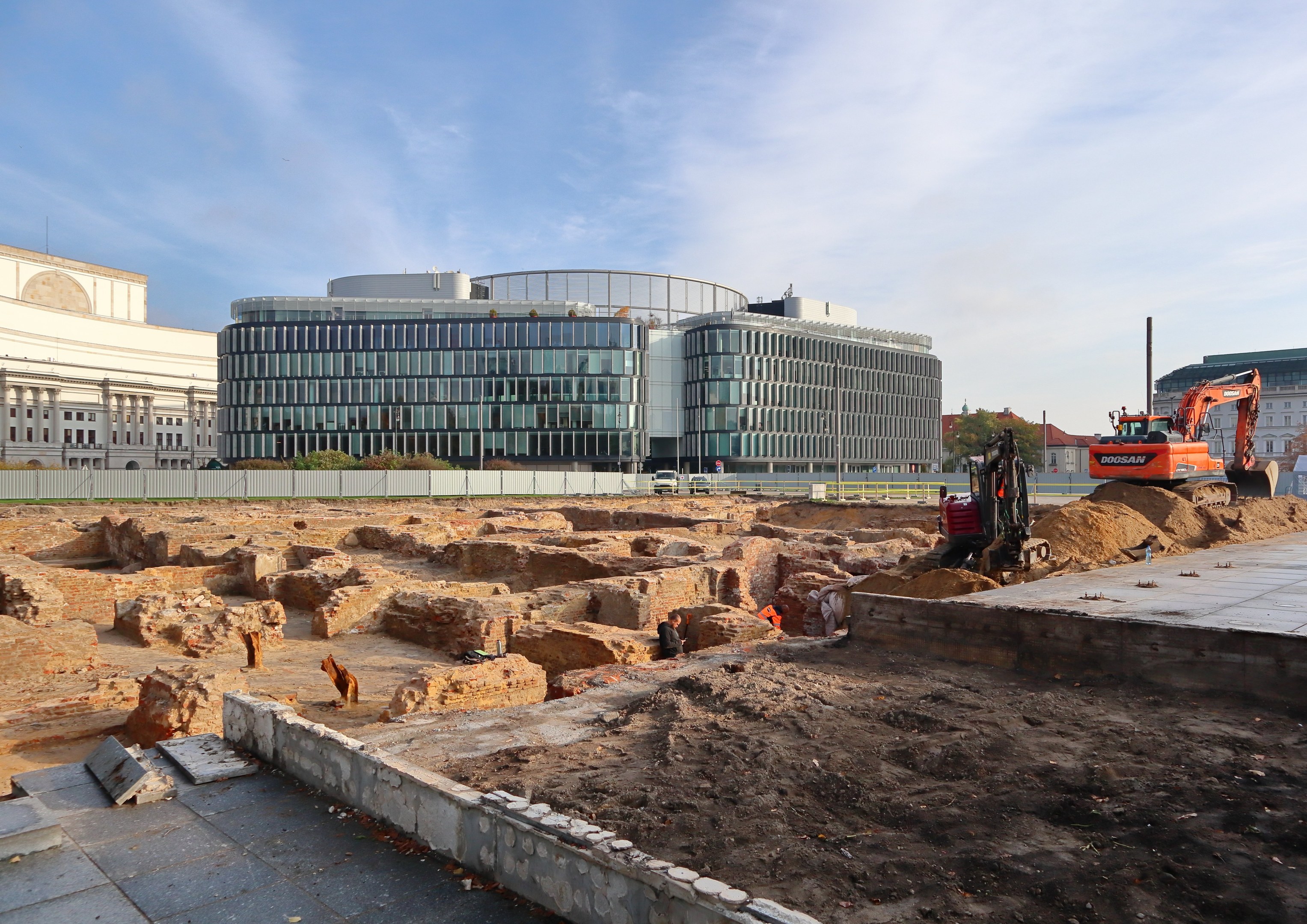 Baustelle in Berlin mit einem großen Gebäude im Bau, Fahrzeugen, Arbeitern und Materialien, vor einem bewölkten Himmel, das den Bau der Berliner Mauer zeigt.