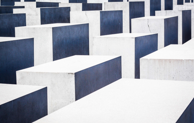 Luftaufnahme des Holocaust-Mahnmals für die ermordeten Juden Europas in Berlin, die zahlreiche weiße und blaue Betonsteine in einem Gittermuster zeigt.
