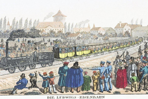 Gruppe von Menschen um ein stehendes Zug auf den Schienen mit einigen Passagieren im Zug und anderen außerhalb des Zuges, vor einem Hintergrund von Gebäuden und Bäumen, mit der Bildunterschrift "Ludwigs-Eisenbahn, die erste Bahnstation in Deutschland" unten.