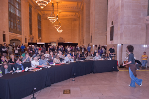 Ein Konzertbild mit einer Menge Menschen, einem Mann, der auf der rechten Seite Gitarre spielt und singt, einer Wand und Fenstern im Hintergrund, Lichtern oben und einem Boden unten.