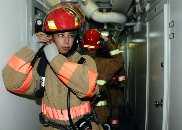 Feuerwehrleute in Uniform in einem Raum mit Rohren und Gegenständen während eines Trainings.