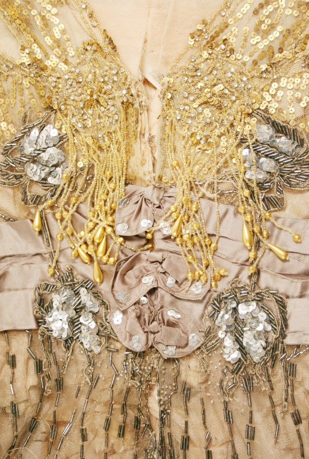 Ein Close-up eines hellen Kleides mit goldenen Pailletten, die funkeln, und Perlen, die Eleganz verleihen.