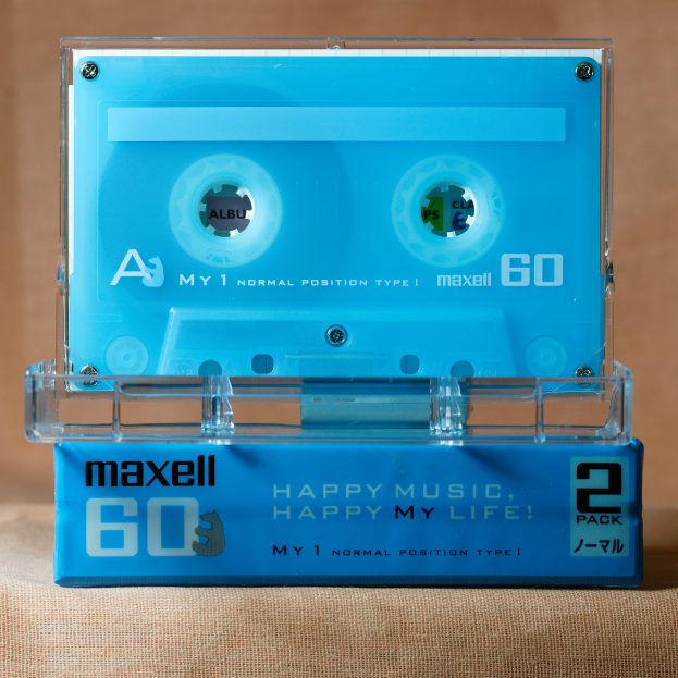 Blaue Kassette mit der Aufschrift "Maxell Happy Music, Happy My Life" auf einer braunen Oberfläche.