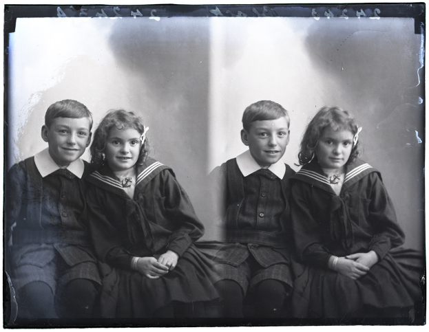 Vier Kinder in Schuluniformen, zwei Jungen und zwei Mädchen, die fröhlich in einem Schwarz-Weiß-Foto posieren.