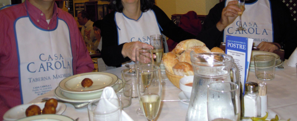 Menschen sitzen an Tischen mit Tellern, Geschirr, Besteck, Brotkörben, Gläsern und einer Werbung.