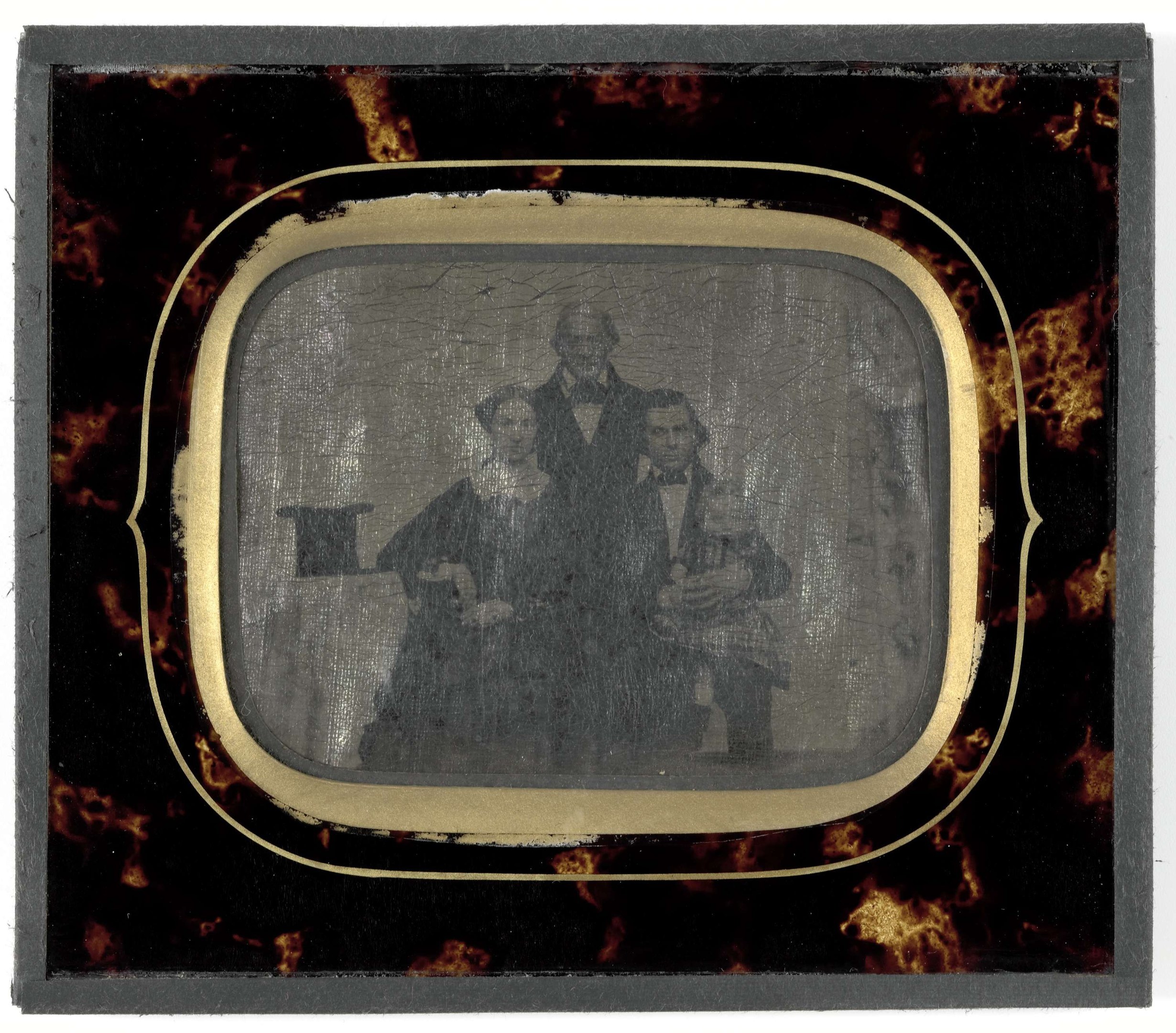 Ein Schwarz-Weiß-Foto eines Mannes in Anzug und Krawatte und einer Frau in unbekannter Kleidung, die ernst vor einem alten Fernseher gegen einen weißen Hintergrund stehen.