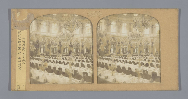 Ein altes Foto eines prächtigen Hotel-Speisesaals mit Tischen, Stühlen, Kronleuchtern und Fenstern, auf dem links ein Schild mit der Aufschrift "Sale a Manger, Grand Hotel" zu sehen ist.