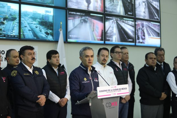 Eine Gruppe von Männern steht vor einem Podium mit einem Mikrofon und einer Tafel mit der Aufschrift "Mexikanische Zoll- und Grenzschutzbehörde", mit Fernsehgeräten und einer Flagge dahinter.