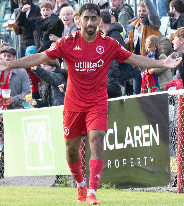 Ein Fußballspieler in roter Uniform rennt auf einem Feld mit ausgestreckten Armen, umgeben von Zuschauern im Hintergrund, mit einem Banner mit der Aufschrift "Middlesbrough FC gegen Swansea City - Sky Bet Championship" im Vordergrund.