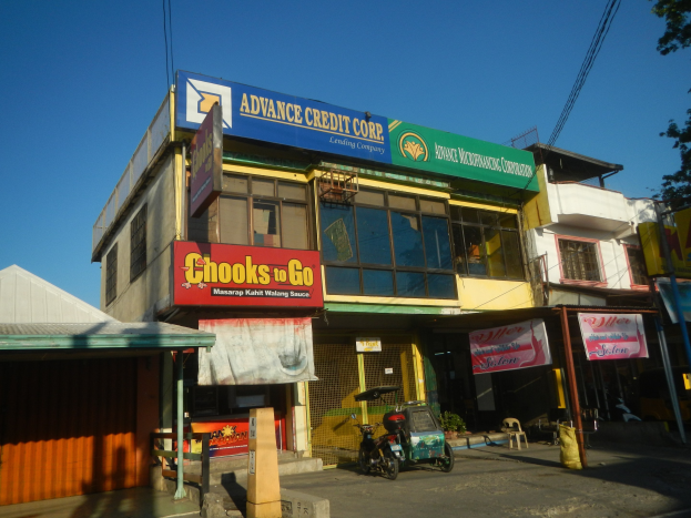 Ein Gebäude mit einer Tafel, auf der "Advance Credit Corp" steht, auf einer Straße mit Fahrzeugen, Werbetafeln, Strommasten und Bäumen unter einem klaren Himmel.
