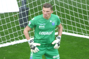 Ein Torwart in grüner Uniform steht vor einem Fußballtor auf saftigem Grün, mit Handschuhen.