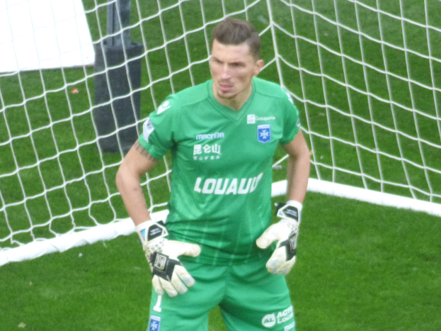 Ein Torwart in grüner Uniform steht vor einem Fußballtor auf saftigem Grün, mit Handschuhen.