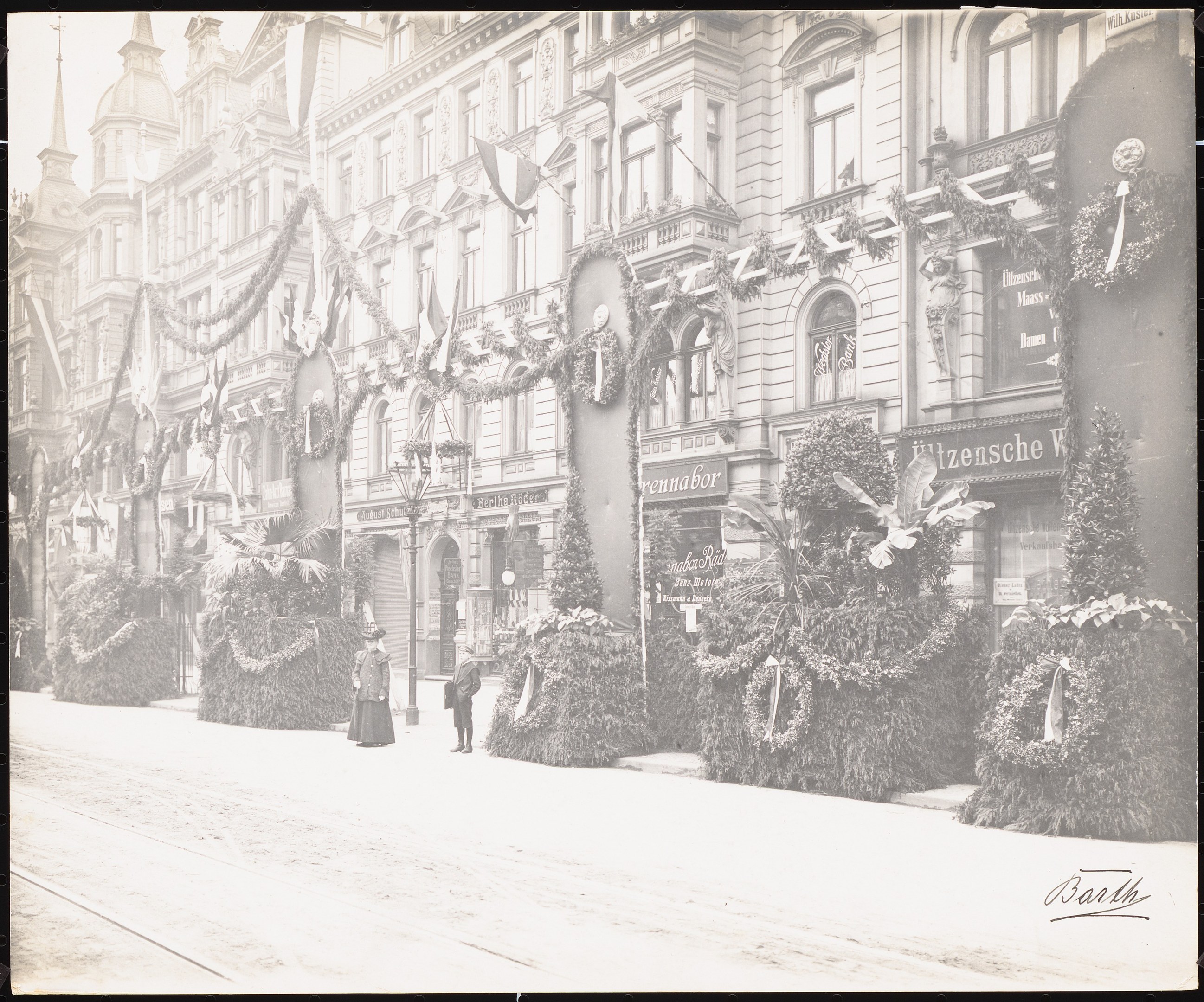 Schwarzes und weißes Foto einer Stadtstraße mit Fußgängern, Gebäuden mit Fenstern, Pflanzen, Flaggen und Namensschildern und einer Straße unten.