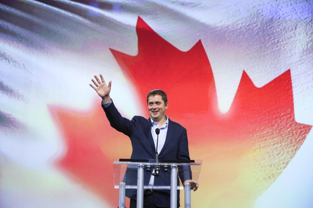 Der kanadische Premierminister Alex Salmond steht an einem Podium mit Mikrofonen, lächelt vor einer kanadischen Flagge und hat einen Bildschirm im Hintergrund.