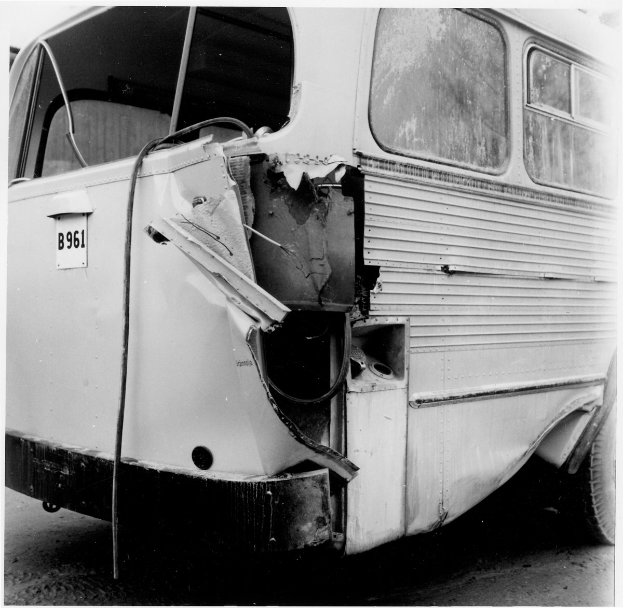Schwarz-weißes Foto eines Busses mit schwerer Frontschaden nach einer Autokollision, der auf der Straße liegt.