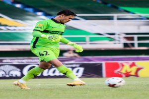 Ein Torwart in grünem Trikot kickt einen Fußball auf einem Rasenfeld, im Hintergrund sind Banner mit "Chivas USA vs Mexico City, 3-1, Copa Libertadores" und Tribünen zu sehen.