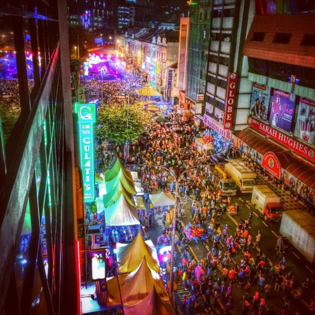 Eine volle KarnevalsSzene mit Zelten, Buden, Gebäuden und Bannern, die die Straße säumen, mit leuchtenden Lichtern im Hintergrund.