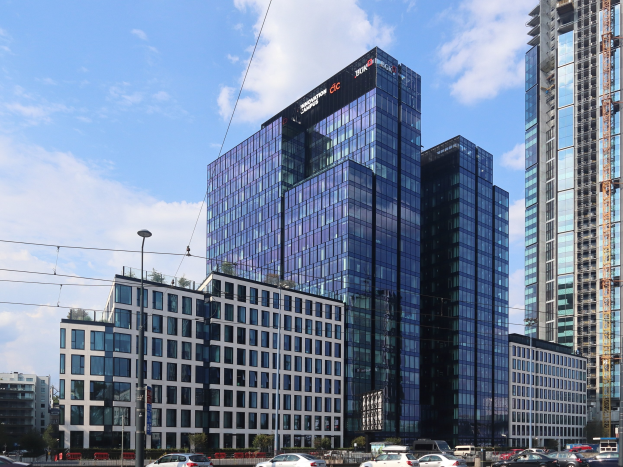 Headquarters of Deutsche Bank in Frankfurt, Germany, a large multi-windowed building surrounded by urban infrastructure and greenery under a cloudy sky.