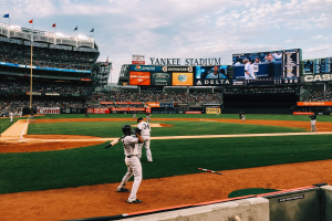 Baseballspiel im Yankee Stadium mit Spielern auf dem Feld und Zuschauern in den Rängen, umgeben von Stadionmerkmalen unter einem bewölktem Himmel.